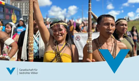 Demozug mit zwei Personen im Vordergrund. Sie tragen traditionellen Schmuck.